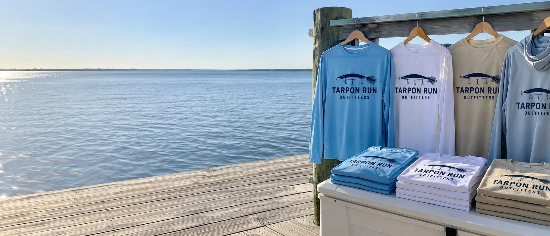 Custom printed fishing shirts on hangers along a weathered dock railing